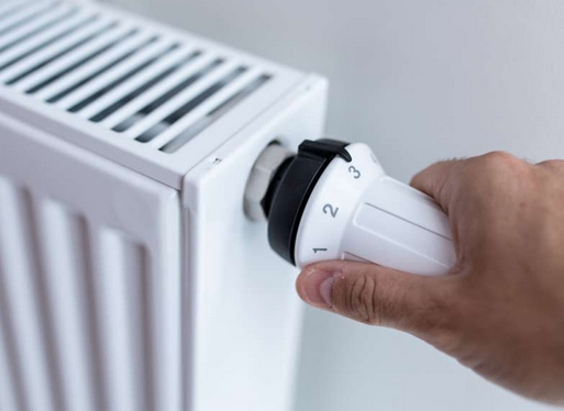 A hand adjusts a thermostat on a white radiator with a scale of 1 to 3.