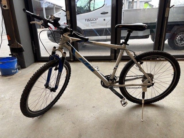 Ein Fahrrad steht in einem Geschäft mit einem weißen Lieferwagen davor. Das Fahrrad hat einen blau-silbernen Rahmen und sein Vorderrad ist leicht angehoben.