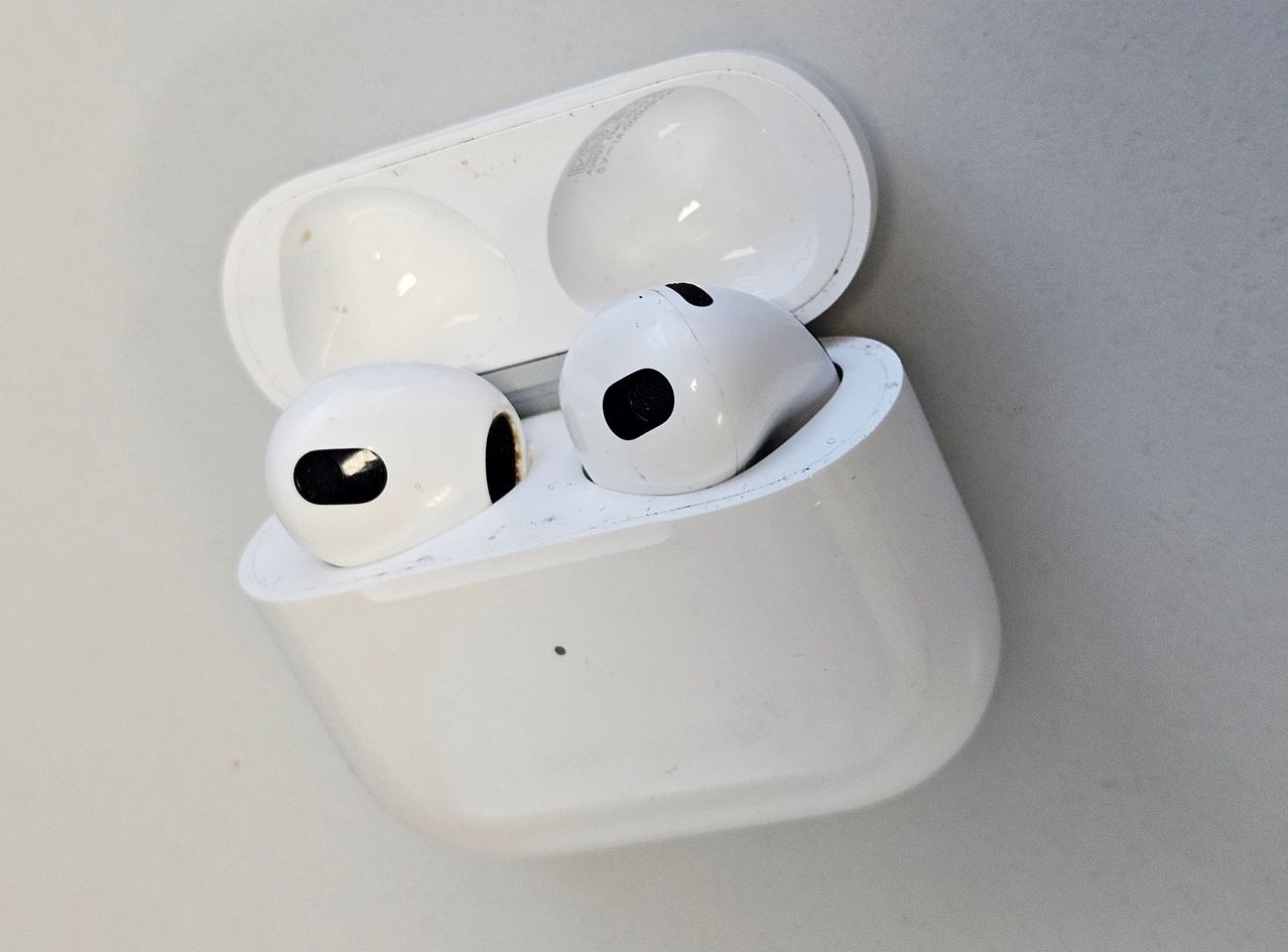 Eine weiße Ladebox für kabellose Kopfhörer mit zwei weißen Kopfhörern darin. Jeder Kopfhörer hat schwarze Punkte und wirkt leicht abgenutzt.