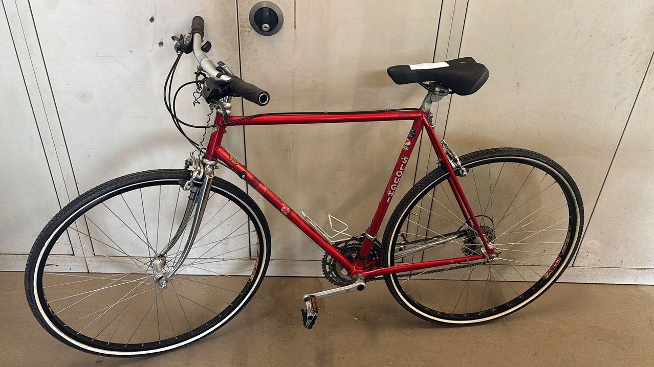Ein rotes Fahrrad mit schwarzem Sattel steht gegen eine weiße Wand. Das Fahrrad ist ein Solo-GHI-Modell.