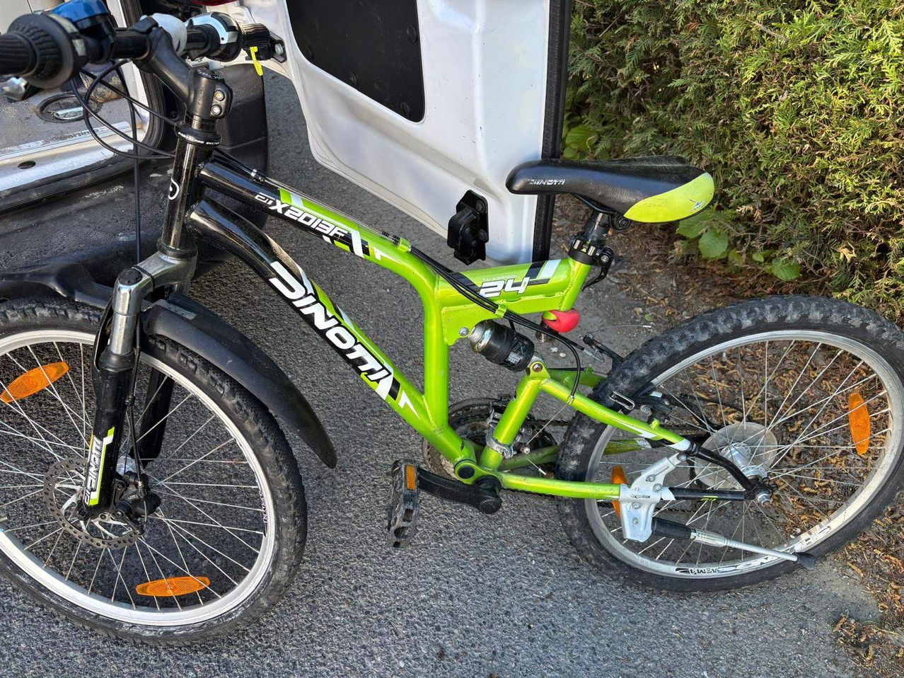 A green bicycle with the word 'DINOM' on the side. It has a black seat and a white door behind it.