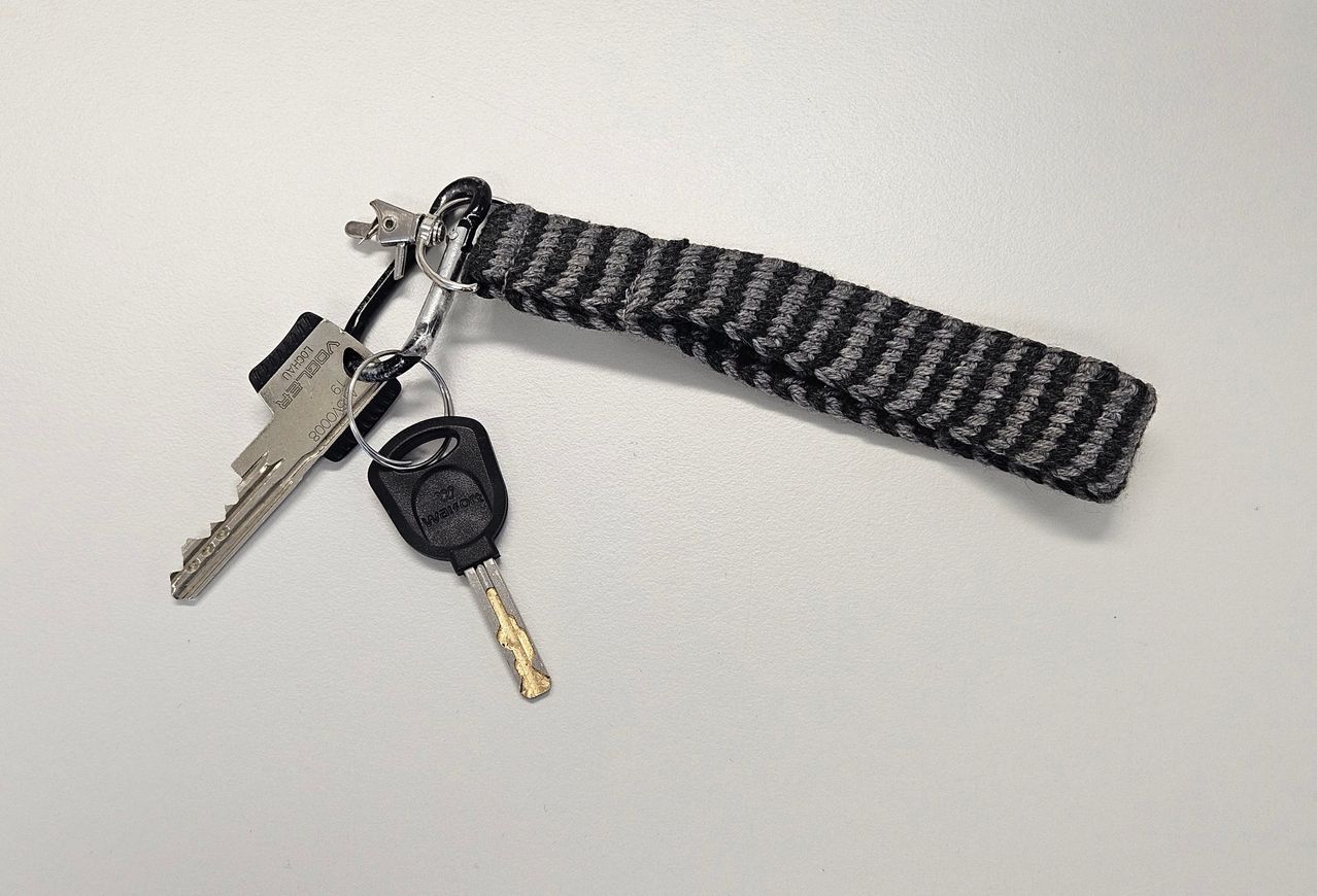 A set of car keys with a silver carabiner on a gray and black knitted strap on a white background.
