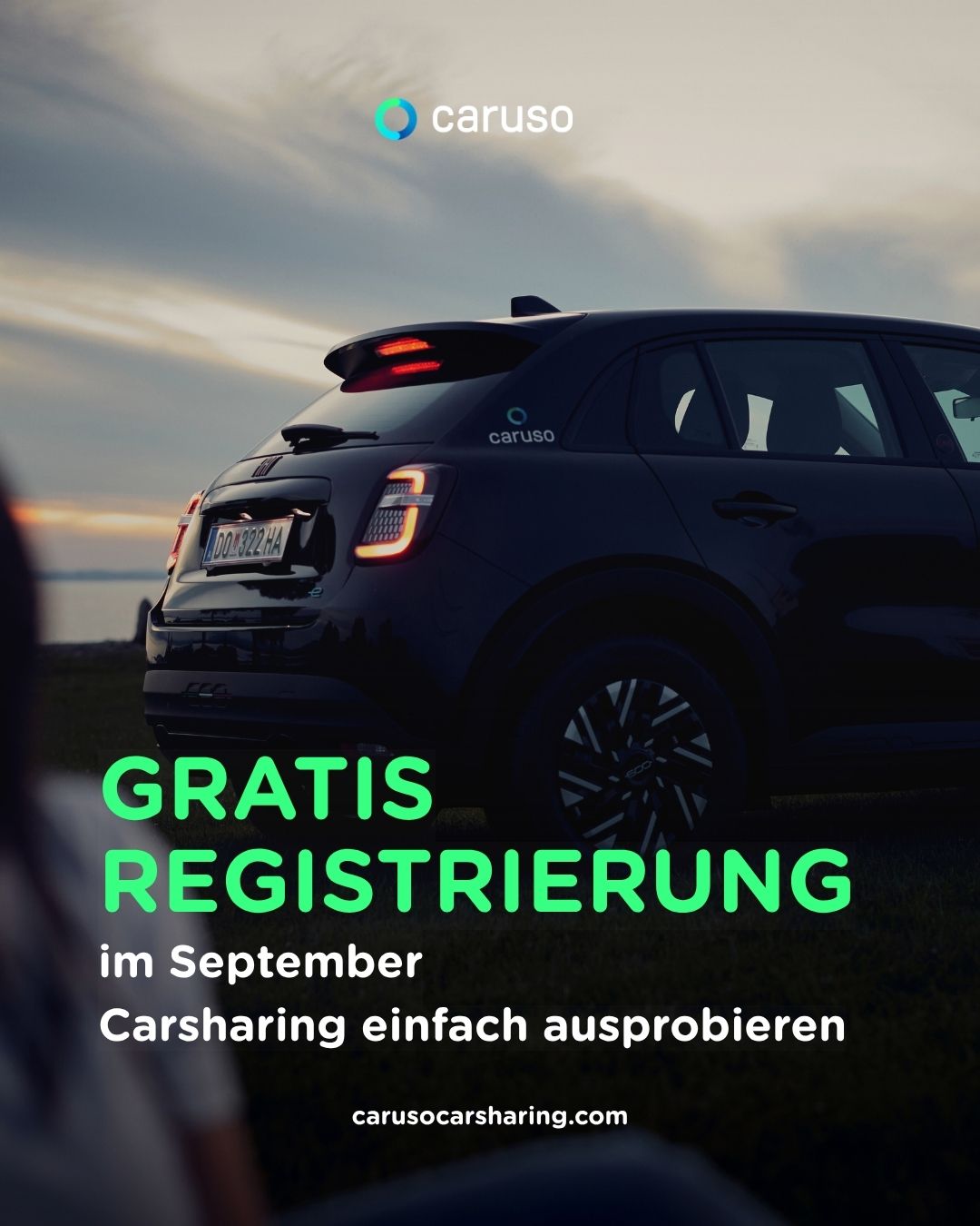 A black car with the text 'GRATIS REGISTRIERUNG im September' and 'Carsharing einfach ausprobieren' is parked in a grassy area. The car has a license plate with the text 'DD 322 HA'. The car's back lights are on. The sky is cloudy.