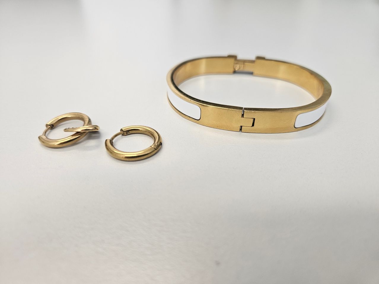 A gold-tone bracelet with a white stripe and two matching gold-tone hoop earrings on a white surface.
