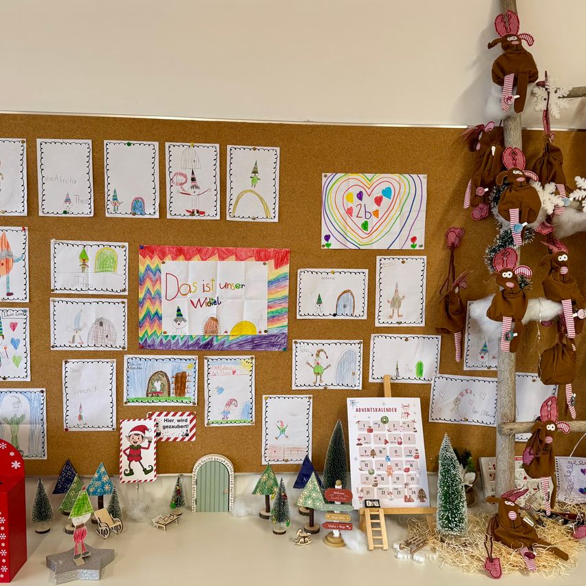 Eine Pinnwand zeigt bunte Zeichnungen und Bastelarbeiten. Darunter ist ein Adventskalender mit Bäumen und Figuren aufgebaut. Gefüllte Tiere hängen von einem Ast ab.