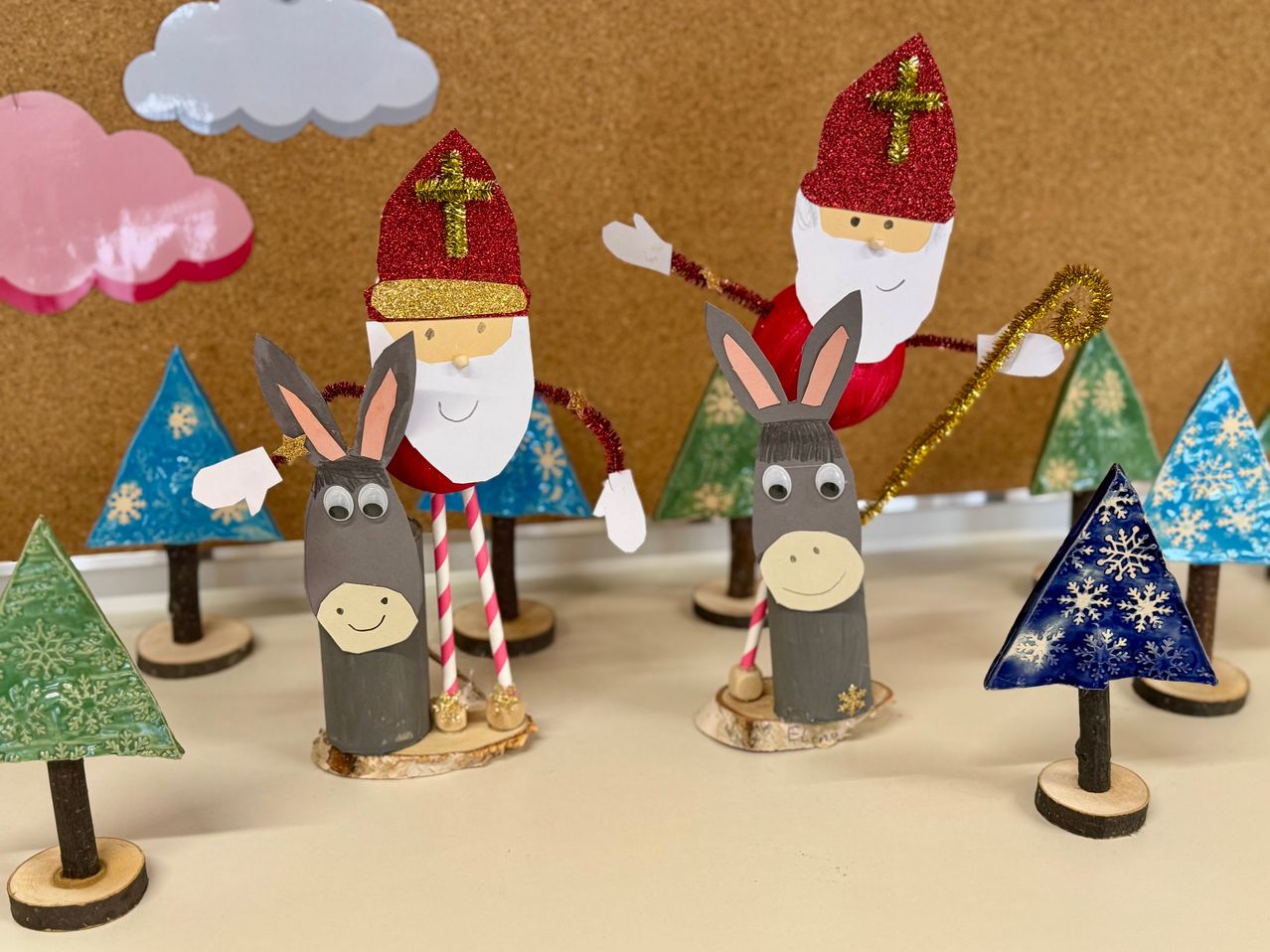 Drei Weihnachtsdekorationen zeigen eine Weihnachtsmann-Figur mit rotem Hut, einen Esel und einen schneebedeckten Tannenbaum. Die Weihnachtsmann-Figur hält einen Stab, und die Esel haben bunte Strohhalme im Maul.