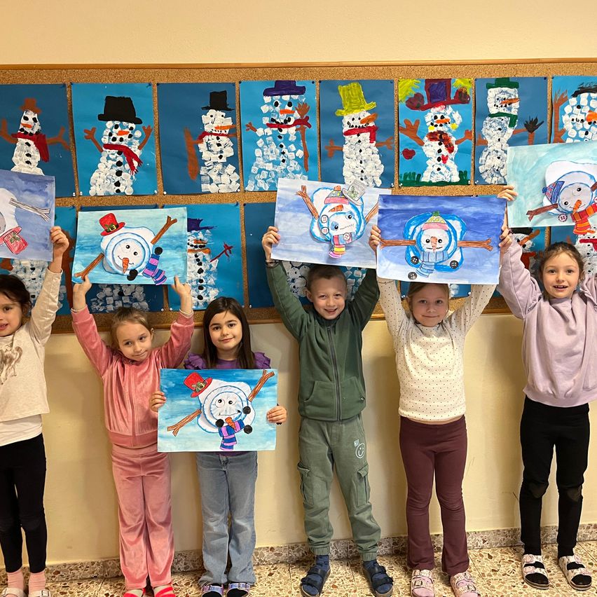 Eine Gruppe von Kindern, die ihre Schneemanngemälde vor einer Wand hochhalten, auf der Schneemänner gemalt sind.