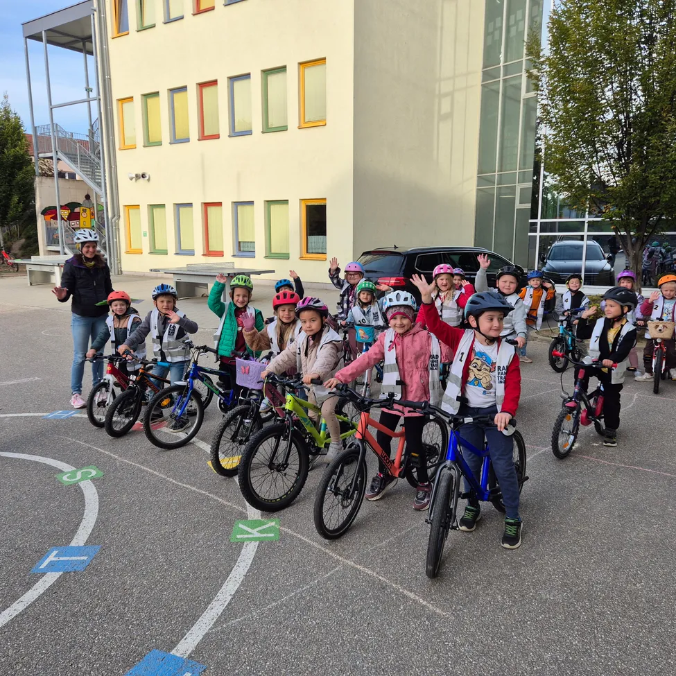 Eine Gruppe von Kindern mit Helmen fährt in einem Kreis auf Fahrrädern vor einem Gebäude.
