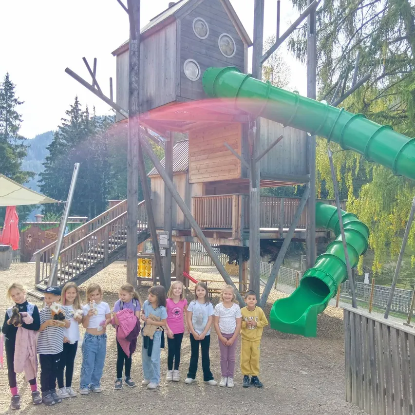 Eine Gruppe von Kindern steht vor einem hölzernen Spielhaus mit einer grünen Rutsche.
