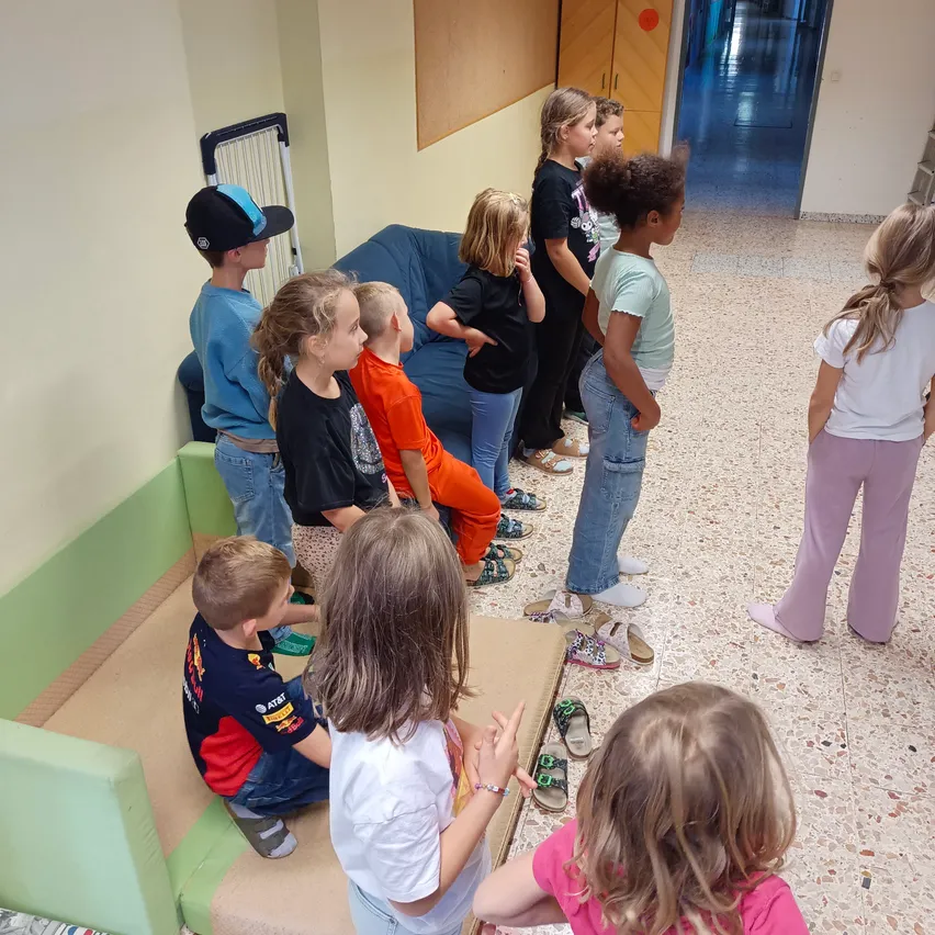 Eine Gruppe von Kindern versammelt sich in einem Raum, einige sitzen auf einer Couch, andere stehen herum.