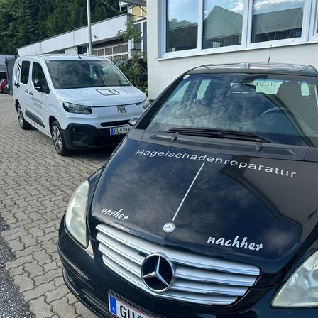 Zwei Autos sind auf einer Ziegelfläche geparkt, eines ist ein weißer Lieferwagen und das andere ist ein schwarzer Mercedes-Benz mit Hagelschadenreparatur auf der Motorhaube.