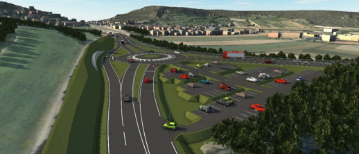 Eine Luftaufnahme einer Autobahn mit mehreren Spuren, Fahrzeugen und einem Kreisverkehr. Die Landschaft umfasst Grünflächen, Berge und eine Stadt in der Ferne.