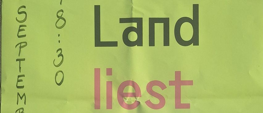 Ein grünes Poster an einer Wand zeigt den Text 'Das Land liest' in Rot und Schwarz. Darunter befindet sich der kleinere Text 'Geschichte erzählen.' Links ist eine Adresse 'Aktiv wohnen, Grabengasse 9' zu sehen, rechts steht 'Wie Literatur & Wissenschaft Geschichte erlebbar machen.'