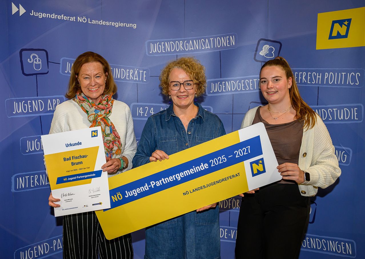 Drei Frauen stehen vor einem Hintergrund mit Text. Die mittlere Frau hält ein großes Zertifikat, die anderen beiden halten kleinere Zertifikate. Der Hintergrund trägt die Aufschrift Jugendorganisationen und Jugendgesetzentwurf.