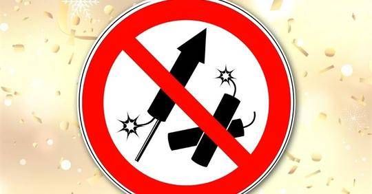 Ein kreisförmiges Schild mit rotem Rand verbietet Feuerwerk und zeigt gekreuzte Symbole einer Rakete und einer Bombe auf einem festlichen goldenen Hintergrund mit verstreuten Lichtern.