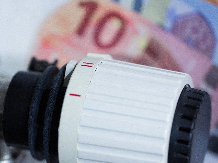 Ein Nahaufnahme eines weißen Thermostats mit einer roten Linie, vor einem unscharfen Hintergrund mit einer 10-Euro-Banknote.