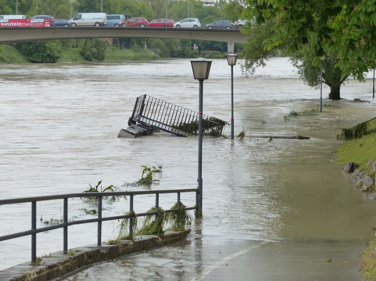 Flooded area with submerged streetlights, a bridge with vehicles, and floating debris.