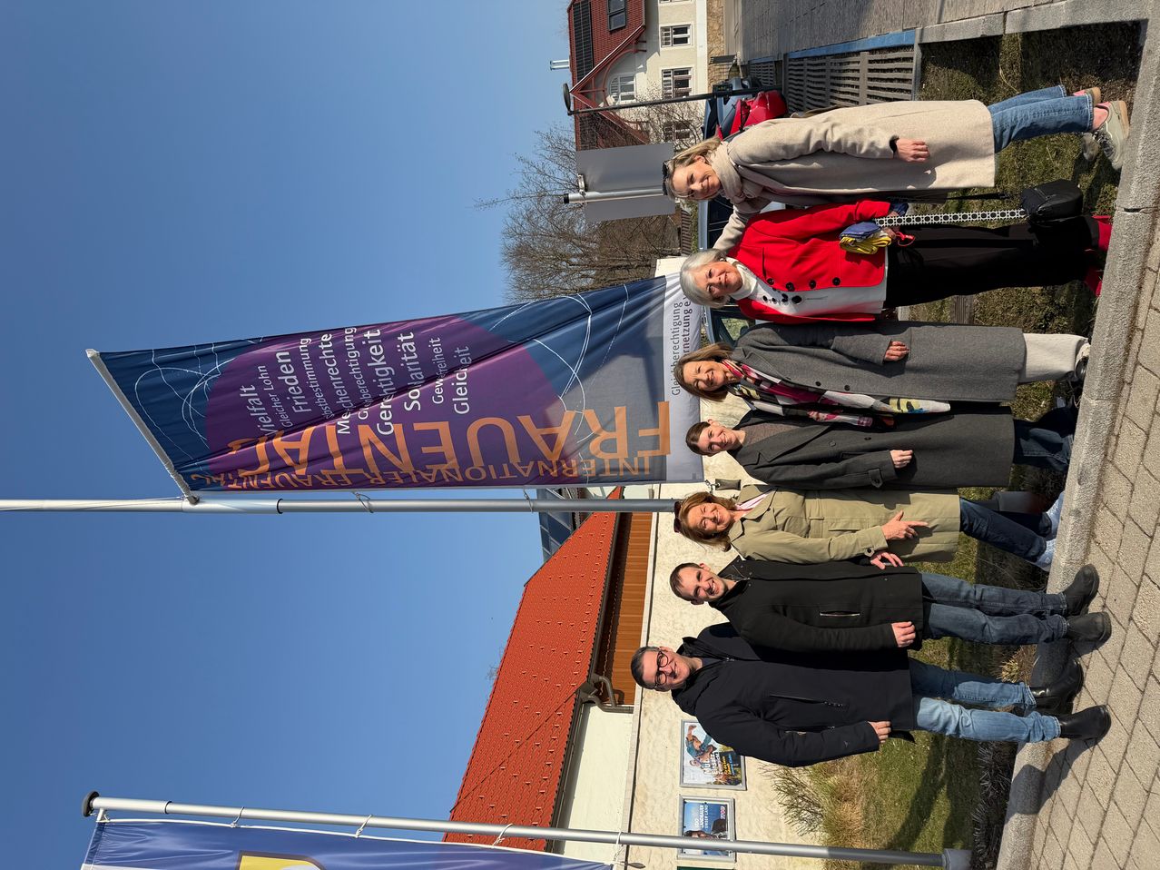 Eine Gruppe von Menschen steht zusammen vor einem Banner, das Heimat steht mit einem Gebäude dahinter.