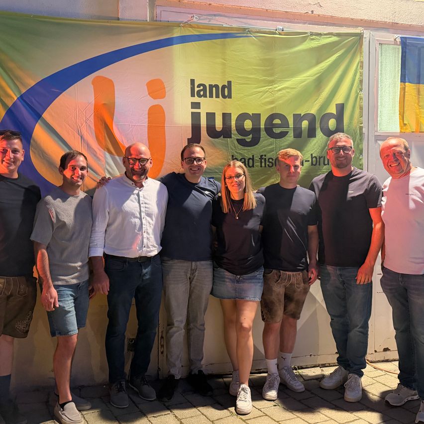 Eine Gruppe von Menschen, sowohl Männer als auch Frauen, steht zusammen vor einem Banner mit einem Logo. Sie alle haben Lächeln im Gesicht.
