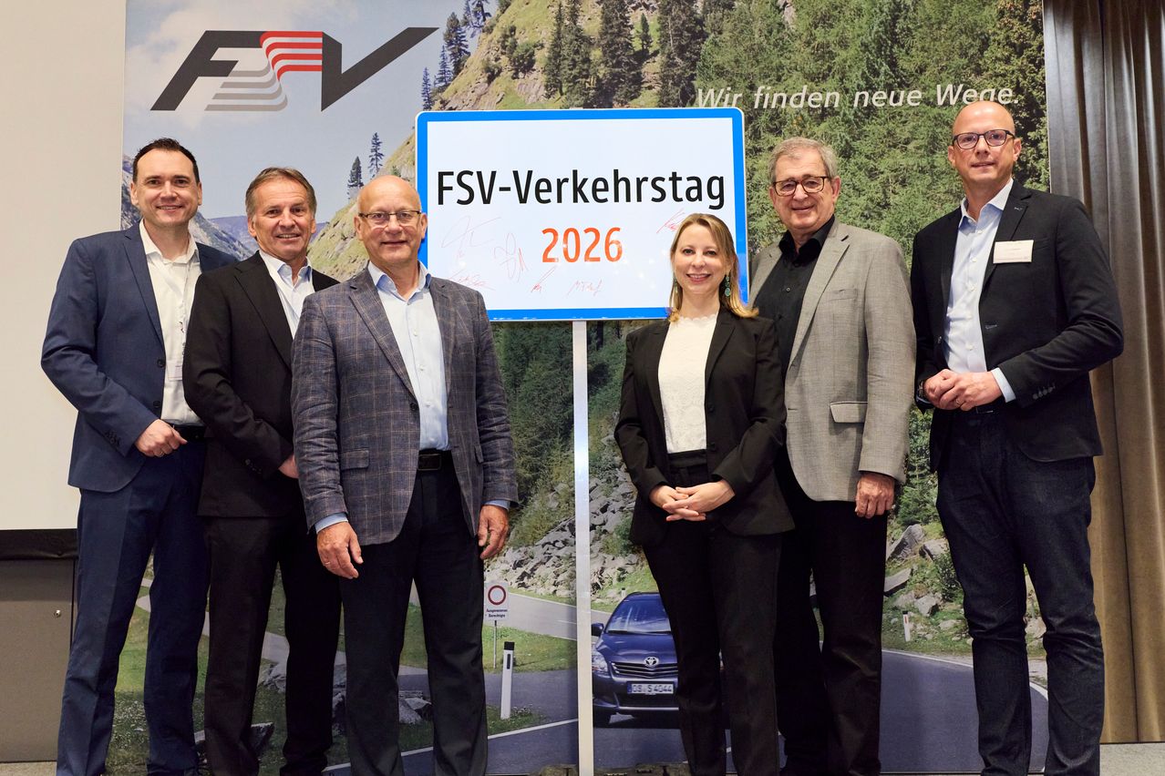 Fünf Männer und eine Frau posieren vor einer Kulisse mit Bergen und einem Schild mit der Aufschrift FSV-Verkehrstag 2026. Der Mann in Karo trägt eine Brille, die Frau in Schwarz hat Ohrringe.