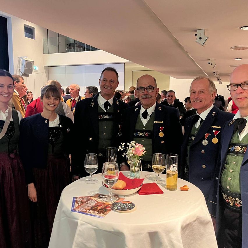 Eine Gruppe von Menschen in formeller Kleidung posiert für ein Foto vor einem Tisch mit Wein glasses und Blumen.