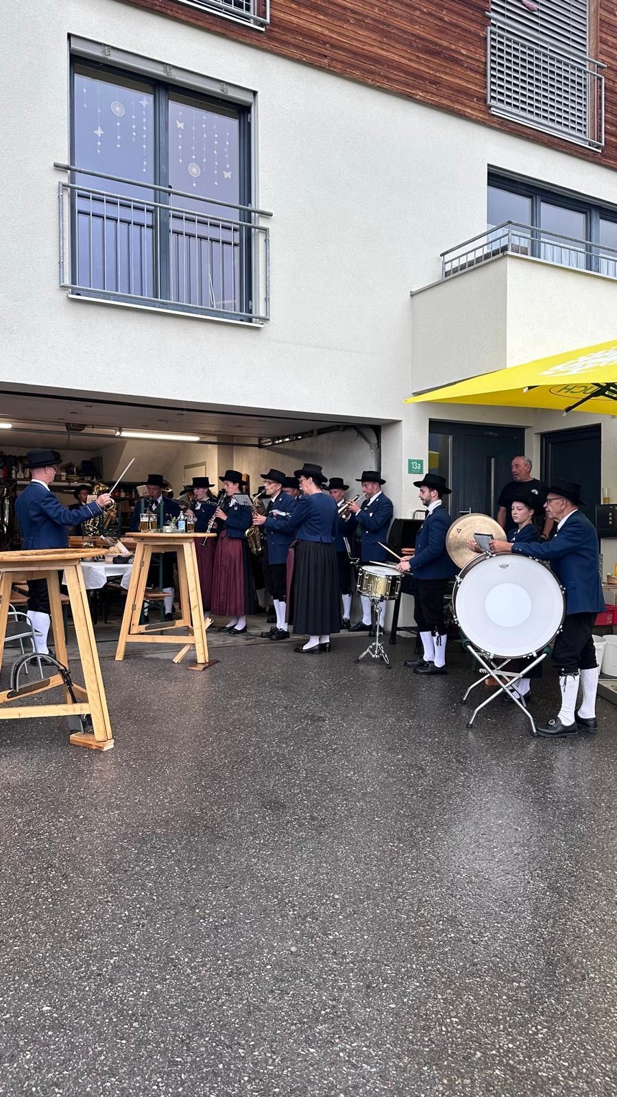 Eine Band in traditioneller Kleidung spielt auf Trommeln und Blechblasinstrumenten vor einem Gebäude.