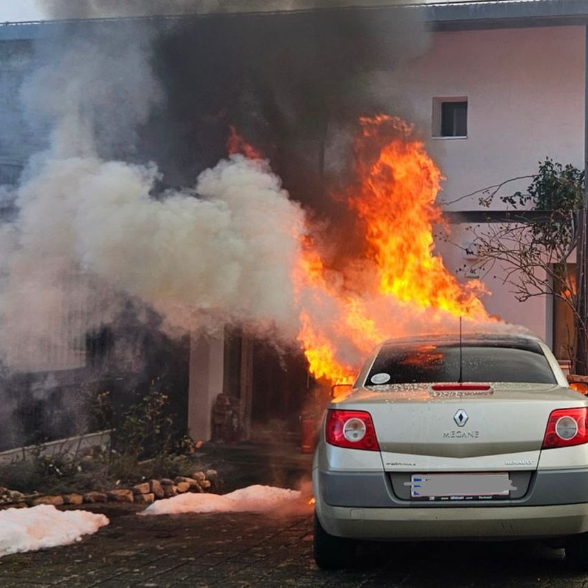 Ein Renault Megane brennt vor einem Haus, wobei Rauch und Feuer aus ihm kommen.