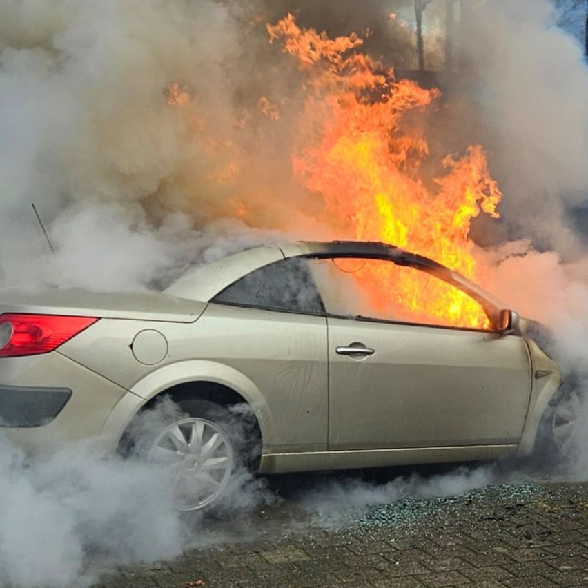 Ein Auto brennt und sendet Flammen und Rauch aus, die Fenster sind zerbrochen und Rauch strömt heraus.