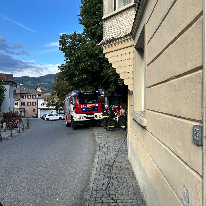 Ein Feuerwehrauto steht am Straßenrand, daneben stehen Feuerwehrleute.