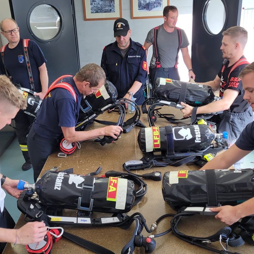 Eine Gruppe Feuerwehrleute versammelt sich um einen Tisch und überprüft und bereitet ihre Ausrüstung vor, einschließlich Sauerstoffflaschen und Schutzausrüstung.