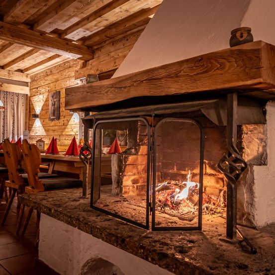 Ein hölzerner Kamin in einem gemütlichen, rustikalen Esszimmer mit brennendem Feuer und einer Holzdecke.
