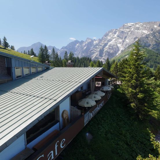 Eine Luftaufnahme eines Cafes mit Metalldach und verschneiten Bergen im Hintergrund.