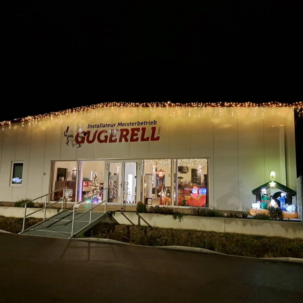 Ein Ladengeschäft mit einem Schild, das 'Gugereill' und Weihnachtsdekorationen zeigt, bei Nacht beleuchtet.