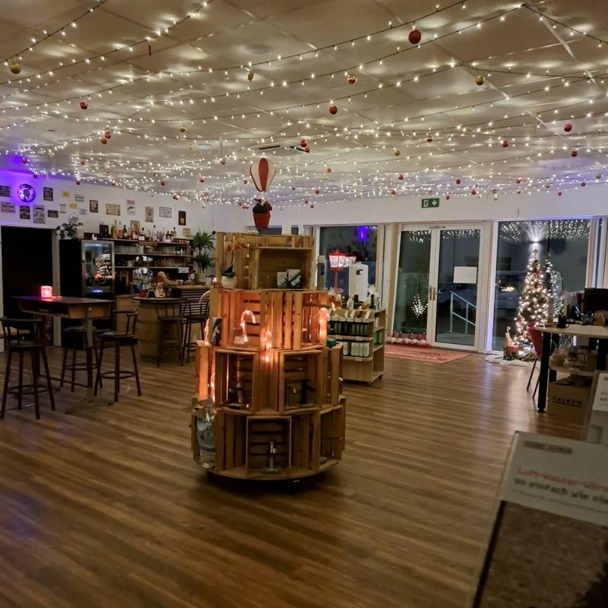 Ein Innenbereich mit Holzböden, geschmückt mit Weihnachtsdekoration. Ein Holzdisplay mit brennenden Kerzen und Regalen mit Flaschen. Ein Weihnachtsbaum und Lichter hängen von der Decke.