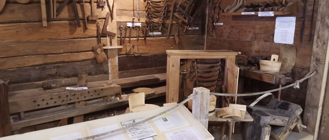 Ein Raum mit hölzernen Werkzeugen und Ausrüstung, einschließlich eines Holztisches mit einer Seilbarriere. Es gibt Holzbänke und Regale mit Werkzeugen an der Wand.