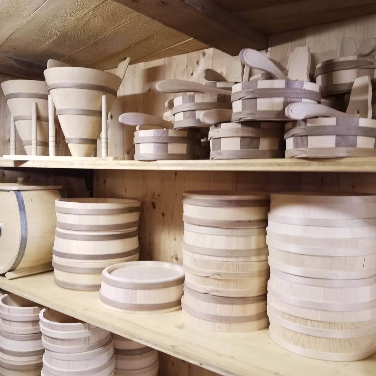 Ein Holzregal gefüllt mit verschiedenen Holzbehältern in unterschiedlichen Formen und Größen, einschließlich Trichter, Fässer und Teller.