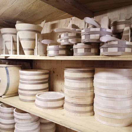 Ein Holzregal gefüllt mit verschiedenen Holzbehältern in unterschiedlichen Formen und Größen, einschließlich Trichter, Fässer und Teller.