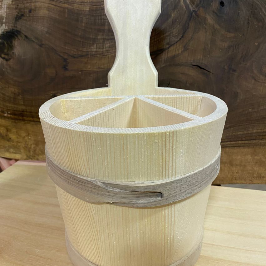 Ein hölzerner Eimer mit Griff, in Fächer unterteilt, ruht auf einer Holzoberfläche.