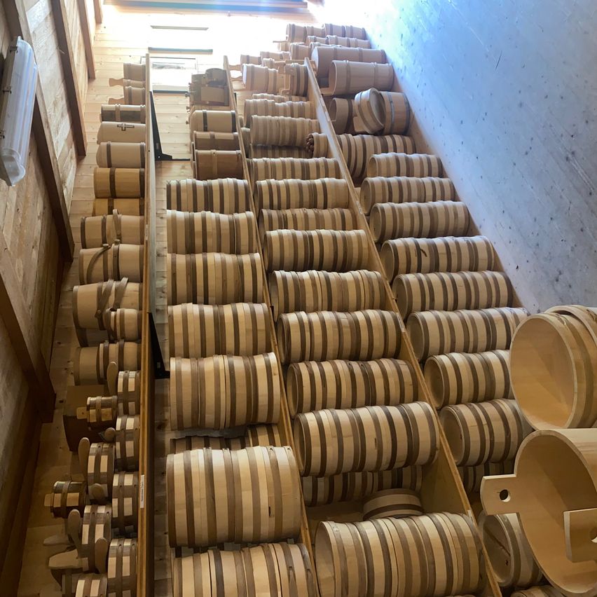 A wooden room filled with rows of barrels with brown and white stripes. A bright light shines from the top left corner.