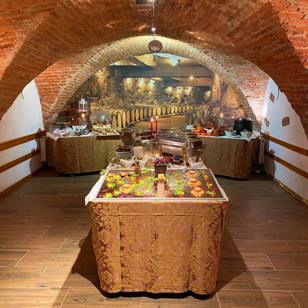Ein Essbereich mit einem gewölbten Ziegelsteindach, das einen Buffettisch mit bunten Speisen, einer Kulisse einer Weinkellerei und brennenden Kerzen zeigt.