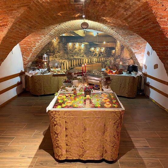 Ein Essbereich mit einem gewölbten Ziegelsteindach, das einen Buffettisch mit bunten Speisen, einer Kulisse einer Weinkellerei und brennenden Kerzen zeigt.