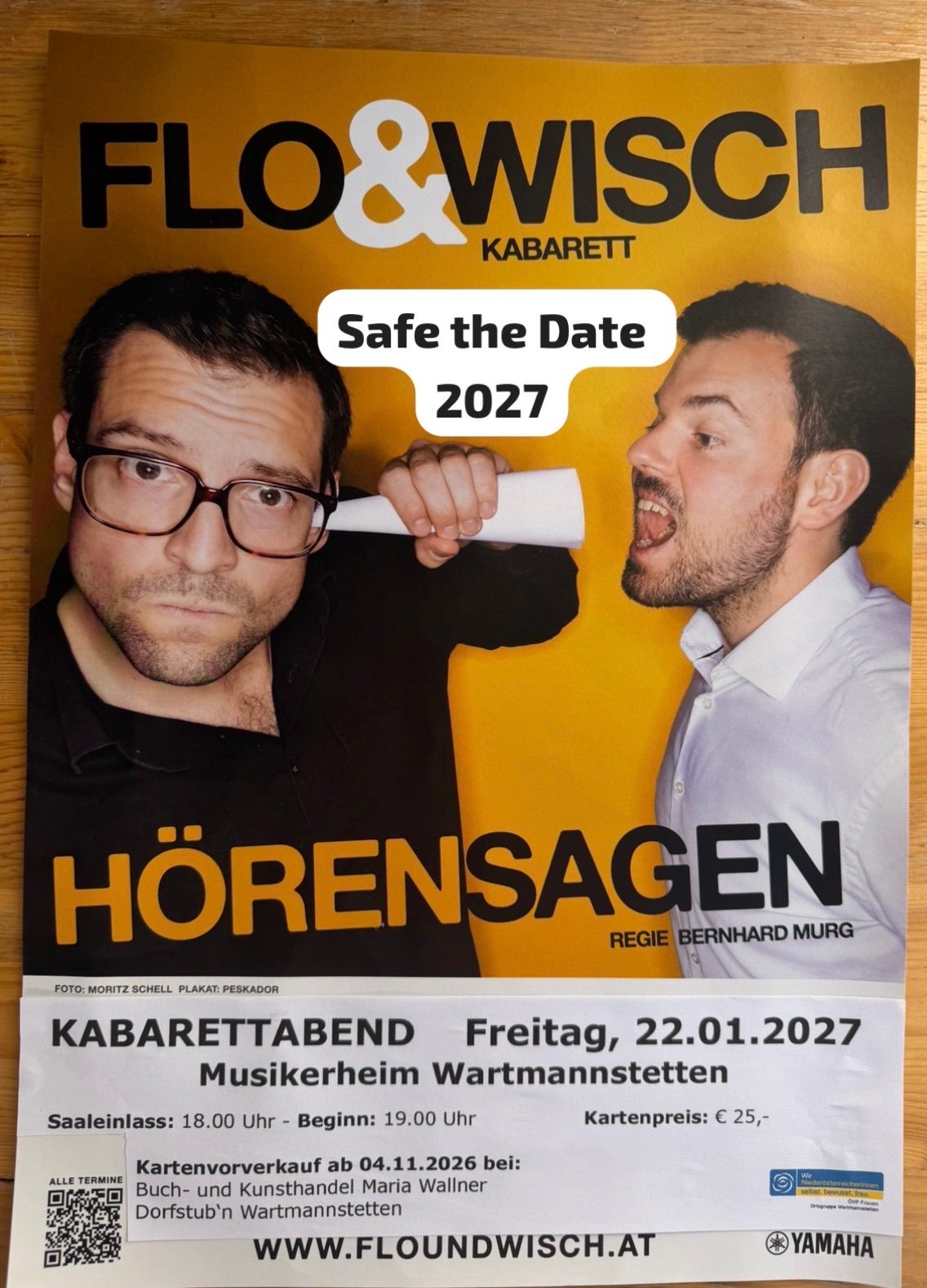 Poster for a comedy event featuring two men. One man holds a rolled paper, while the other looks shocked. The text reads 'Safe the Date 2027' and 'Hörensagen'. The event is scheduled for Friday, January 22, 2027.
