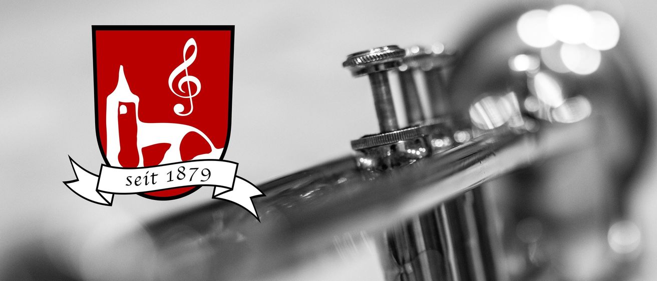 Schwarz-weißes Bild mit einem roten Wappen, das eine Violinschlüssel und die Zahl 79 zeigt. Das Wappen befindet sich auf einem weißen Band vor grauem Hintergrund. Eine Trompete ist ebenfalls sichtbar, mit drei Stimmschlüsseln.