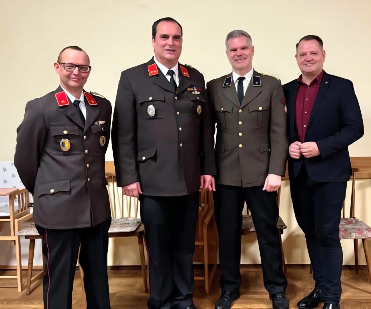 Vier Männer in formeller Kleidung, drei in Militäruniformen und einer in einem dunklen Anzug, stehen lächelnd zusammen. Sie scheinen sich bei einer Veranstaltung zu befinden, möglicherweise einem formellen Treffen.