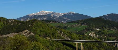 Eine Landschaft mit einer Brücke über einem Tal, mit schneebedeckten Bergen im Hintergrund und einem klaren blauen Himmel.