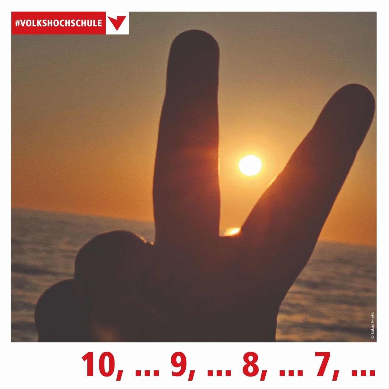 Die Silhouette einer Hand bildet ein Friedenszeichen vor einem Sonnenuntergangshimmel über dem Ozean. Die Sonne ist teilweise von den Fingern verdeckt. Die Zahlen 10, 9, 8, 7 sind in Rot angezeigt.