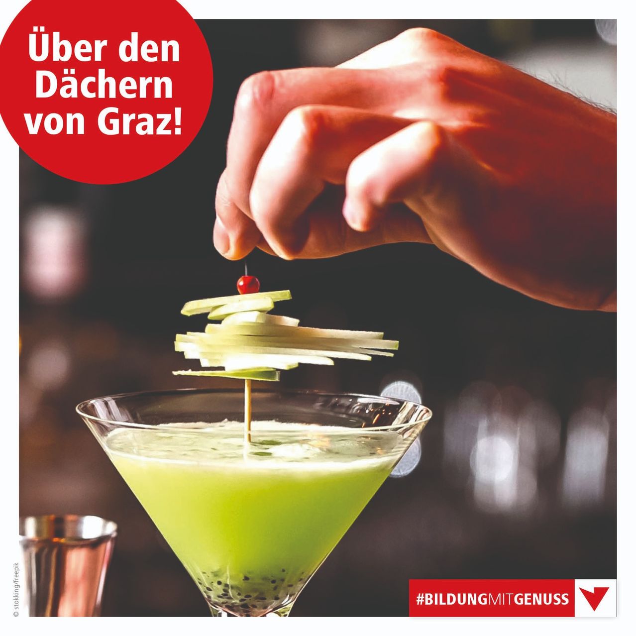 Eine Hand garniert einen grünen Cocktail in einem Martini-Glas mit einem Apfelstück und einer Kirsche. Die Worte 'Über den Dächern von Graz!' sind auf dem Bild zu sehen. #BILDUNGMITGENUSS wird ebenfalls erwähnt.