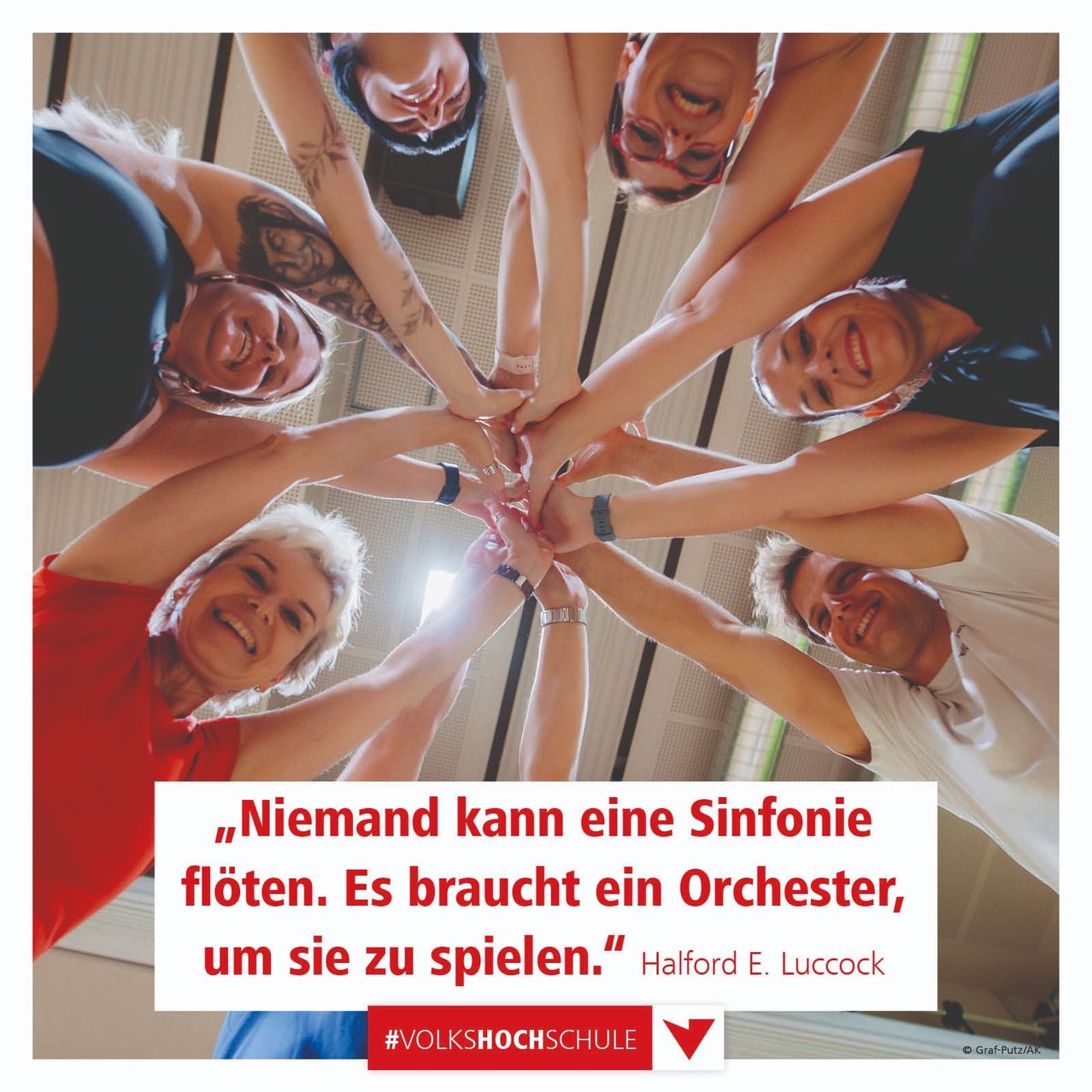 Eine Gruppe von Menschen steht in einem Kreis mit verbundenen Händen und zitiert 'Niemand kann eine Sinfonie spielen. Es braucht ein Orchester,' von Halford E. Luccock.