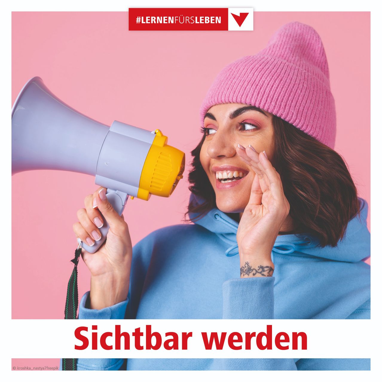 Eine lächelnde Frau hält ein Megaphon in der Hand, trägt eine rosa Mütze und eine blaue Kapuzenjacke. Der Hintergrund ist rosa mit dem Text 'Sichtbar werden' und dem Hashtag '#LERNENFUERSLEBEN'.
