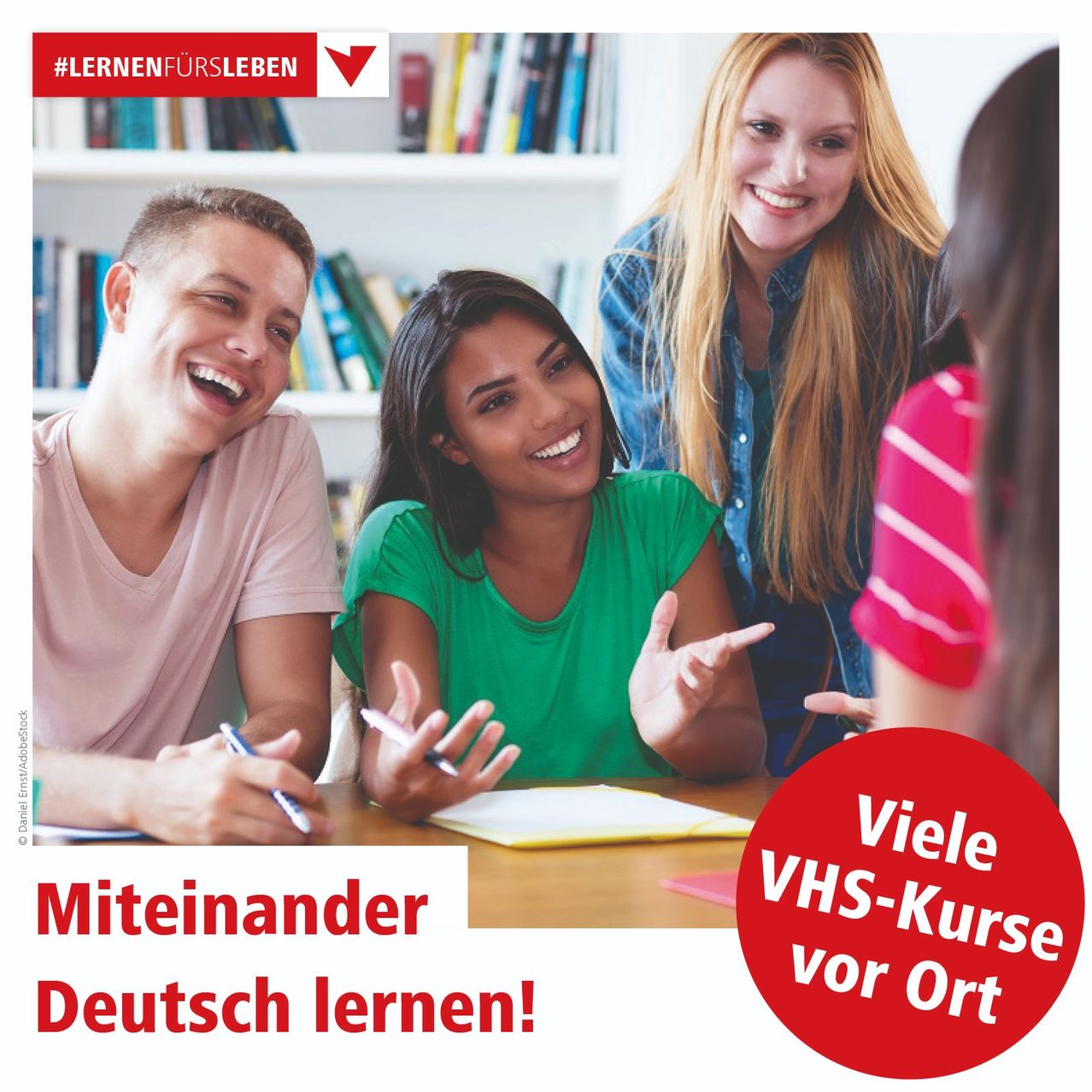 Eine Gruppe von Menschen sitzt um einen Tisch, lächelt und führt ein Gespräch. Eine Frau in Grün spricht mit einem Mann in Rosa. Hinter ihnen schauen zwei Frauen zu. Ein Bücherregal ist im Hintergrund. Die Worte 'Viele VHS-Kurse vor Ort' sind in Rot geschrieben.